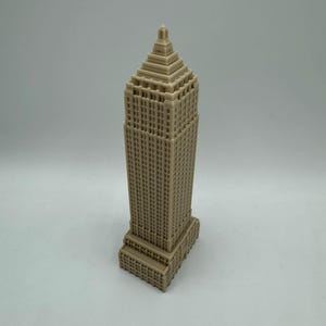 Puede incluir: Un modelo en miniatura beige de un rascacielos alto con un techo puntiagudo y muchas ventanas.