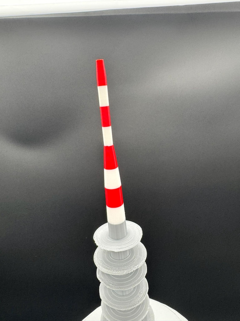 May include: A 3D-printed, abstract sculpture featuring a red and white striped pole atop a stack of translucent, circular platforms. The pole has a red tip and alternating red and white bands. The platforms are stacked, creating a unique, modern art piece.