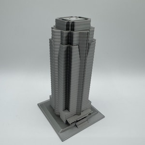 May include: A gray, 3D-printed model of a skyscraper. The building has a rectangular base and a tiered design, with multiple levels and a flat roof. The model is a solid gray color and appears to be made of plastic.