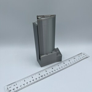 May include: A gray 3D printed model of a skyscraper, approximately 6 inches tall, with a ruler for scale.