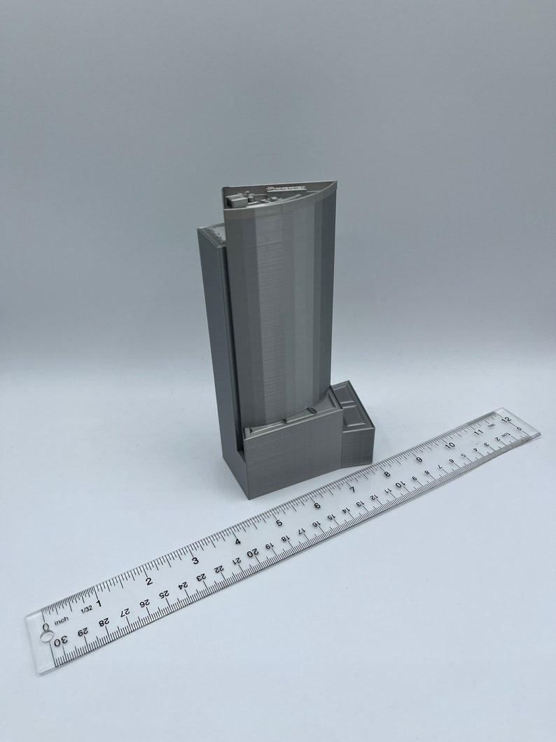 May include: A gray 3D printed model of a skyscraper, approximately 6 inches tall, with a ruler for scale.