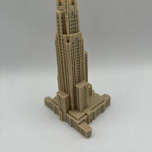 May include: A beige 3D printed model of a tall building with a square base and a tower with many windows.