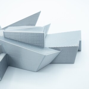 May include: A 3D printed model of a geometric structure with sharp angles and a light gray color.