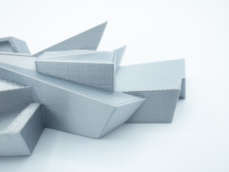 May include: A 3D printed model of a geometric structure with sharp angles and a light gray color.
