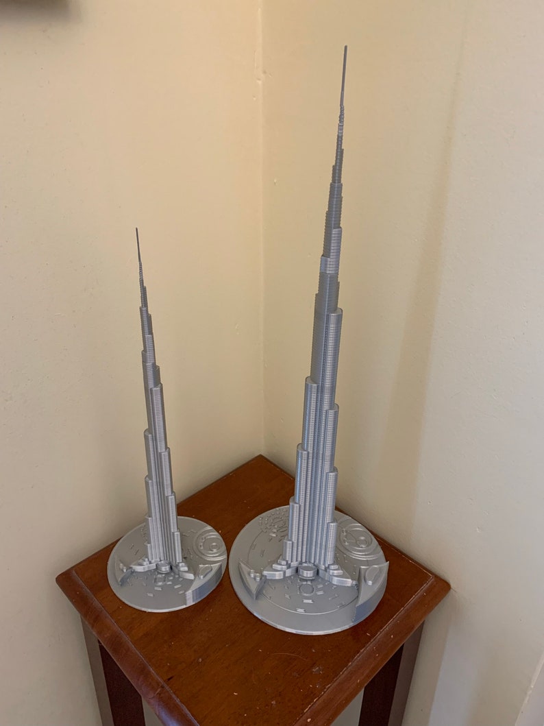 May include: Two silver 3D printed models of the Burj Khalifa, one larger than the other, on a wooden table.