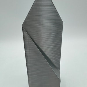 May include: A gray 3D printed model of a tall, slender building with a pointed roof and a geometric design.