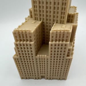 May include: A beige, 3D-printed model of a skyscraper with multiple levels and a detailed facade. The building has a tiered design, with a central tower and surrounding structures. The model is a representation of architecture.