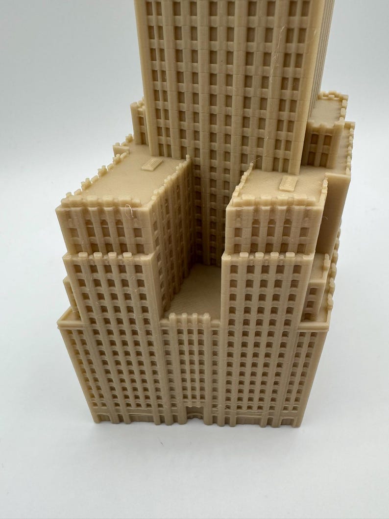 May include: A beige, 3D-printed model of a skyscraper with multiple levels and a detailed facade. The building has a tiered design, with a central tower and surrounding structures. The model is a representation of architecture.