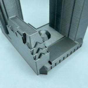 May include: A 3D printed model of a building with a detailed facade and a flat roof. The model is made of a gray plastic and has a textured surface.