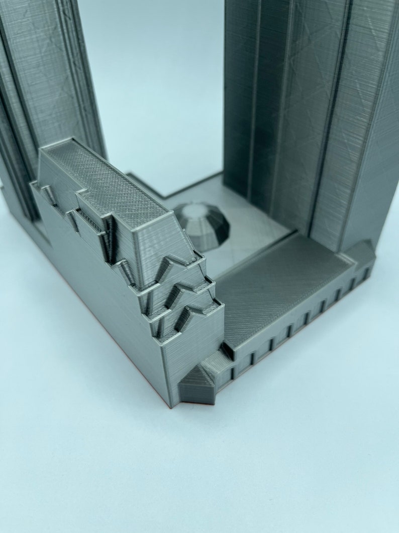 May include: A 3D printed model of a building with a detailed facade and a flat roof. The model is made of a gray plastic and has a textured surface.