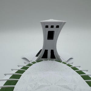 Puede incluir: Maqueta arquitect&oacute;nica blanca que presenta una torre con una abertura rectangular y una estructura abovedada con detalles verdes. La maqueta tiene una superficie texturizada y est&aacute; sobre un fondo liso.