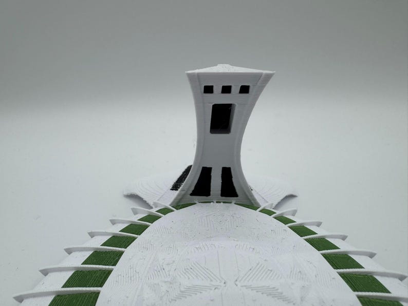 Puede incluir: Maqueta arquitect&oacute;nica blanca que presenta una torre con una abertura rectangular y una estructura abovedada con detalles verdes. La maqueta tiene una superficie texturizada y est&aacute; sobre un fondo liso.