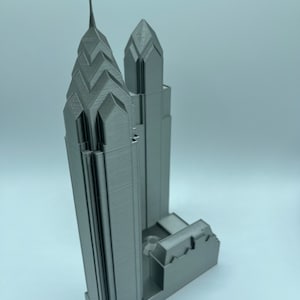 May include: A 3D printed model of a skyscraper with a pointed spire. The model is made of a light gray plastic and is detailed with windows and other architectural features.