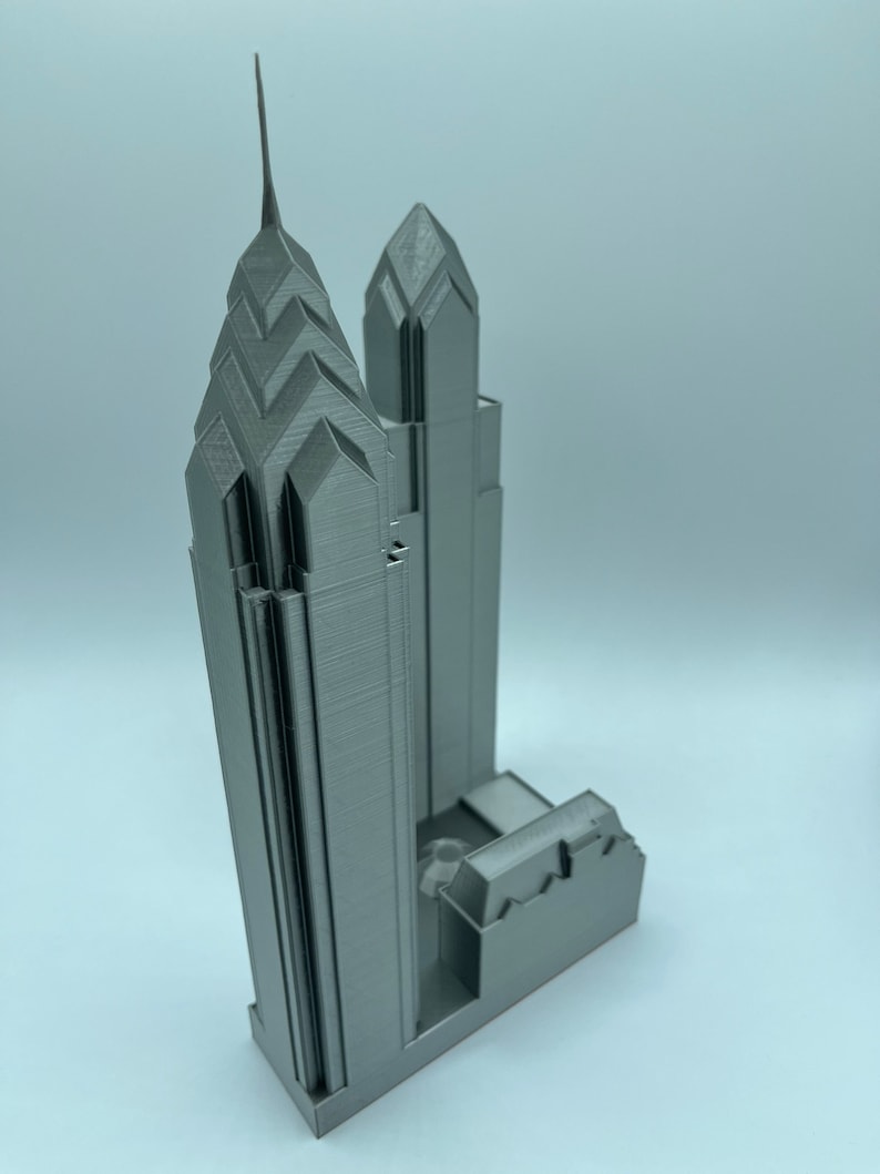 May include: A 3D printed model of a skyscraper with a pointed spire. The model is made of a light gray plastic and is detailed with windows and other architectural features.