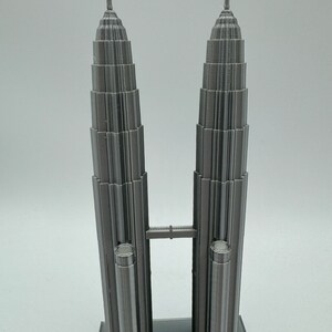 May include: A 3D printed model of the Petronas Towers in Kuala Lumpur, Malaysia. The model is made of gray plastic and features a bridge connecting the two towers.