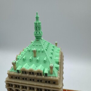 May include: A detailed model of a building with a light green roof and a beige facade. The roof has a textured pattern and several small chimneys. The building's design includes multiple windows and architectural details, showcasing a classic style.