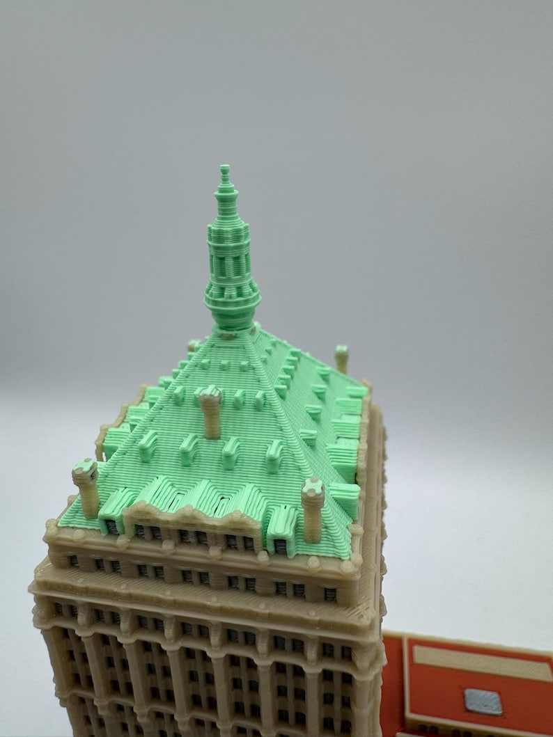 May include: A detailed model of a building with a light green roof and a beige facade. The roof has a textured pattern and several small chimneys. The building's design includes multiple windows and architectural details, showcasing a classic style.