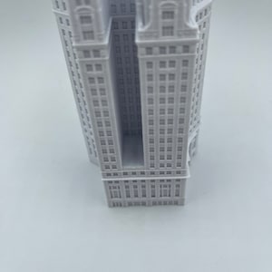 Op de afbeelding: Een wit 3D-geprint model van een hoog gebouw met een rechthoekige opening in het midden.