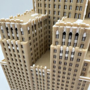 May include: A beige 3D-printed model of a multi-storey building, featuring many windows and architectural details. The model has a layered design with a light facade and white accents, representing a skyscraper. The model is a detailed representation.