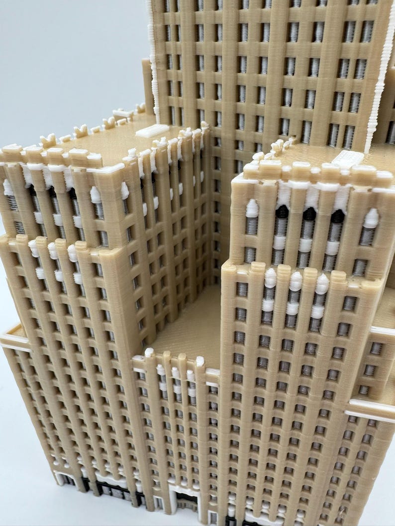 May include: A beige 3D-printed model of a multi-storey building, featuring many windows and architectural details. The model has a layered design with a light facade and white accents, representing a skyscraper. The model is a detailed representation.