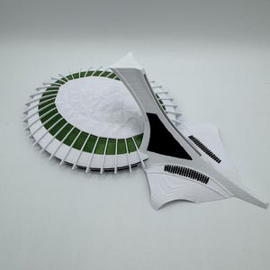 Puede incluir: Maqueta arquitect&oacute;nica blanca y verde. La base circular tiene una superficie blanca texturizada con detalles verdes. Una estructura en forma de ala se extiende desde la base, con detalles negros.