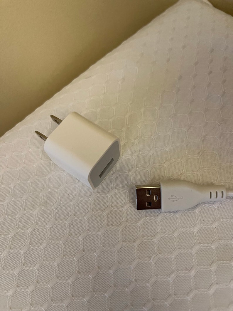 May include: A white wall adapter with two prongs and a USB port, and a white USB cable with a USB-A connector on one end and a USB-C connector on the other end.