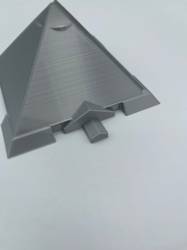 Puede incluir: Modelo de pir&aacute;mide gris impreso en 3D con una superficie texturizada. La pir&aacute;mide tiene una base plana y una peque&ntilde;a estructura que sobresale en un lado. El modelo est&aacute; sobre un fondo blanco.