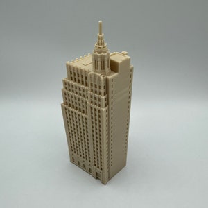 Pu&ograve; includere: Un modello 3D stampato in beige di un edificio alto con una guglia in cima. L'edificio ha molte finestre e una facciata dettagliata.