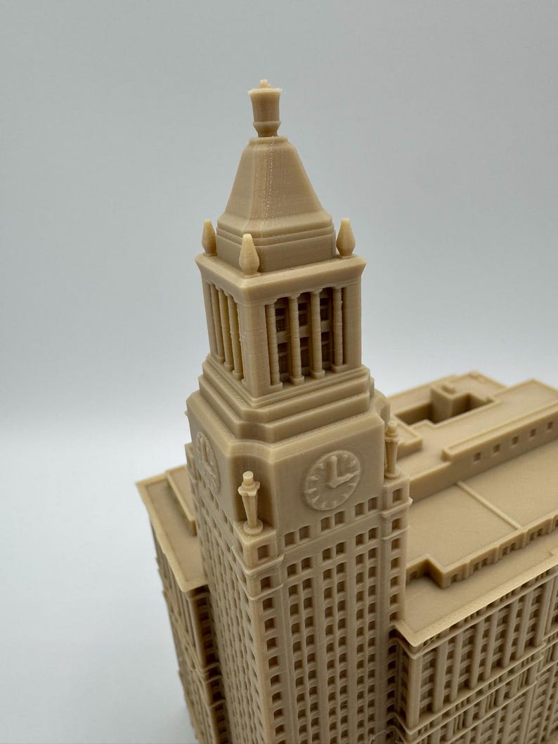 May include: A tan-colored architectural model of a building with a clock tower. The model has detailed windows, columns, and decorative elements. The clock on the tower shows the time as approximately 1:00.