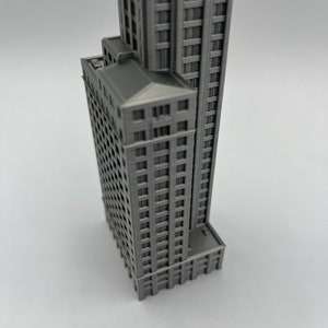 May include: A gray 3D printed model of a tall building with many windows. The model is detailed and realistic, with a flat roof and a base.