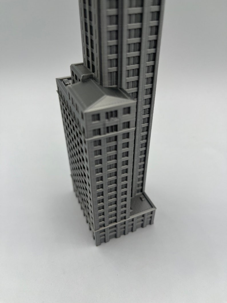 May include: A gray 3D printed model of a tall building with many windows. The model is detailed and realistic, with a flat roof and a base.