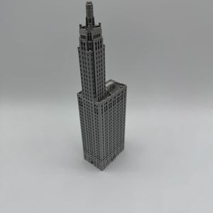 May include: A grey miniature model of a tall skyscraper with a pointed roof and many windows.