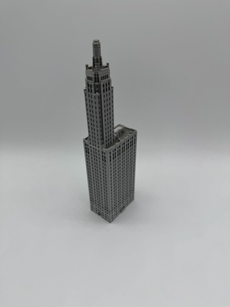 May include: A grey miniature model of a tall skyscraper with a pointed roof and many windows.