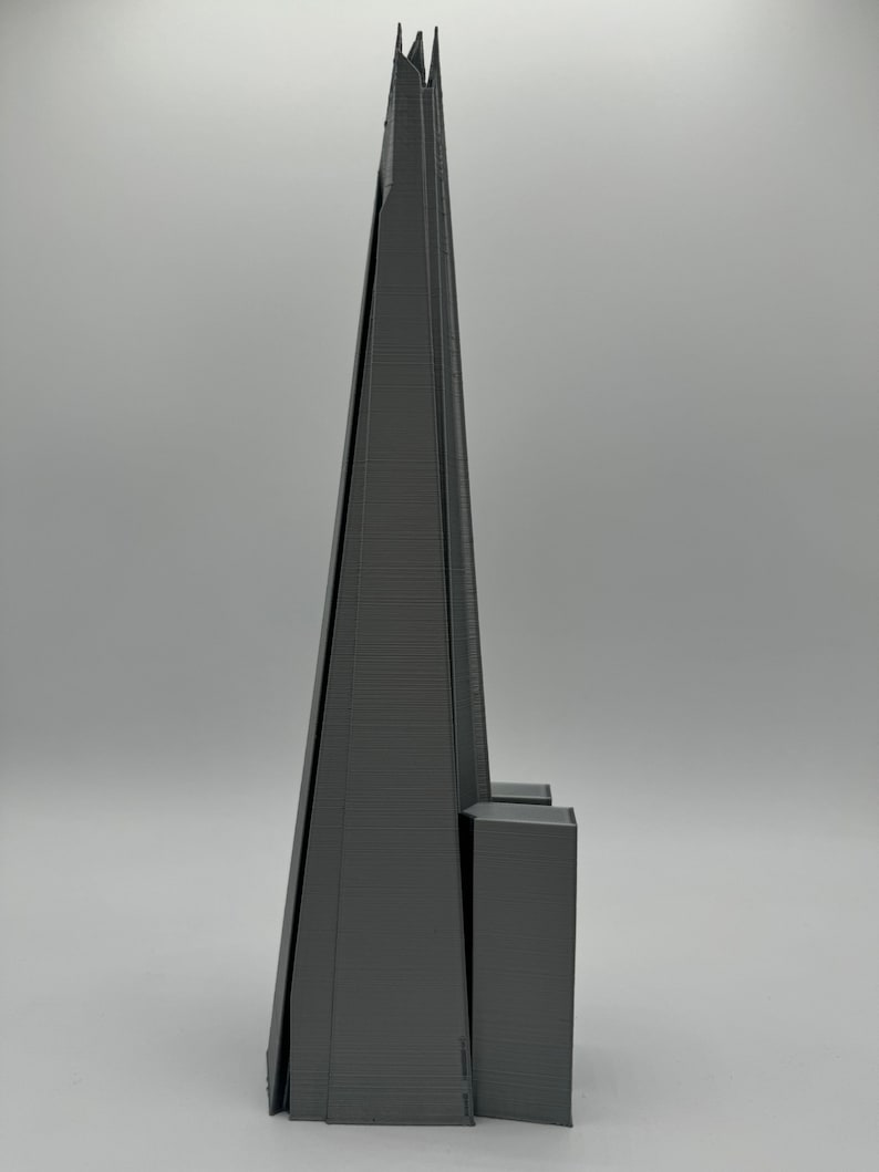 May include: A gray 3D printed model of a skyscraper with a pointed top and a rectangular base.