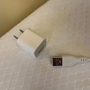 May include: A white wall adapter with two prongs and a USB port, and a white USB cable with a USB-A connector on one end and a USB-C connector on the other end.