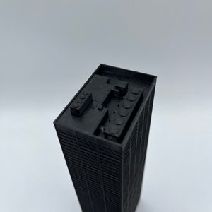 May include: Black 3D printed model of a skyscraper building. The model has a detailed facade and a flat roof with a small structure on top.