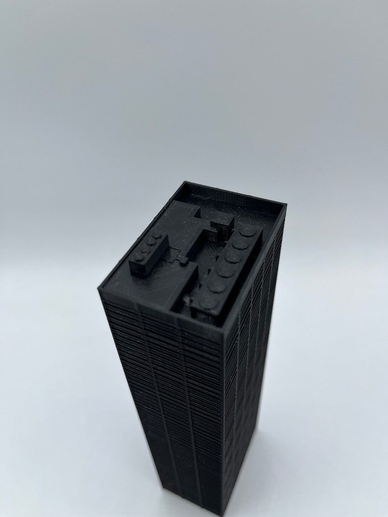 May include: Black 3D printed model of a skyscraper building. The model has a detailed facade and a flat roof with a small structure on top.
