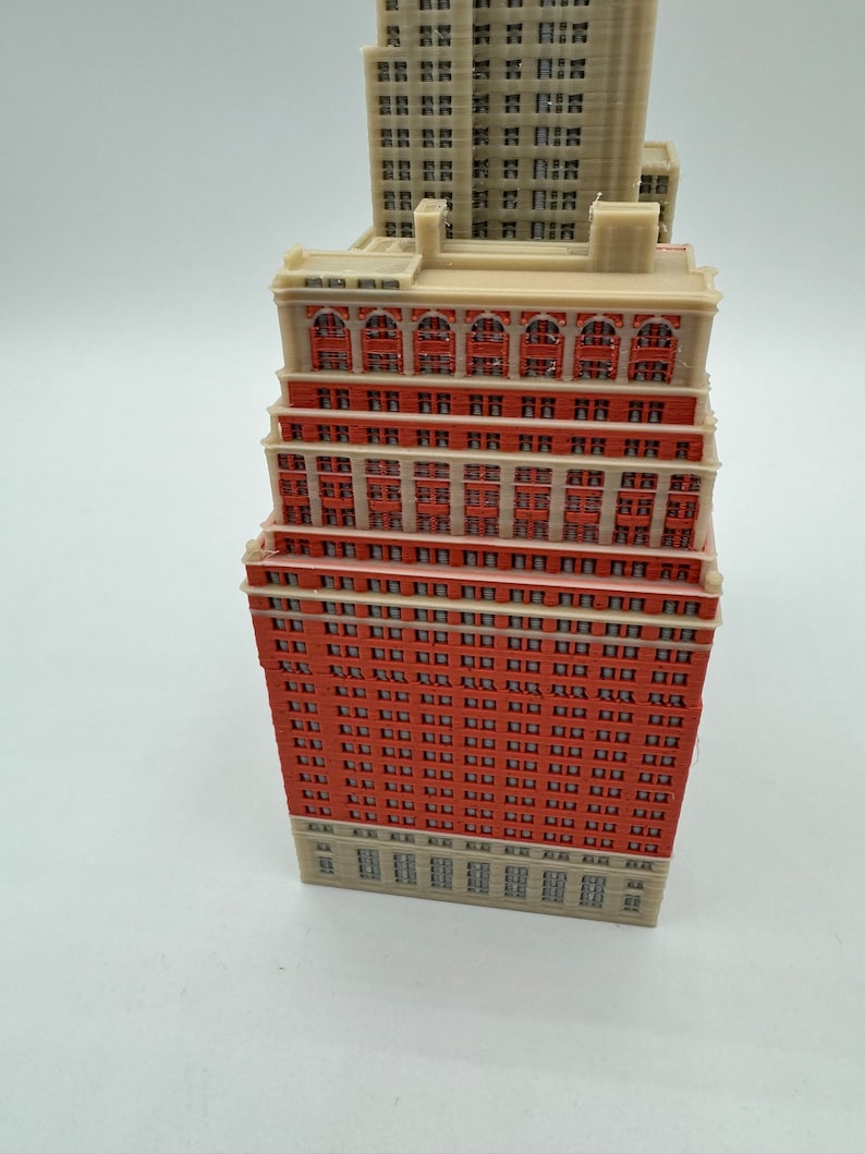 May include: A detailed model of a tall red brick building with many windows. The building has a flat roof and white trim around the windows. The model is made of plastic and is about 25 cm tall.