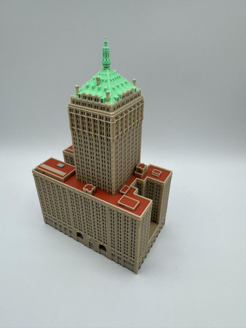 May include: A detailed miniature model of a skyscraper. The building features a tan facade with numerous windows, a red roof, and a green, pyramid-shaped top. The model is a detailed representation of a building.