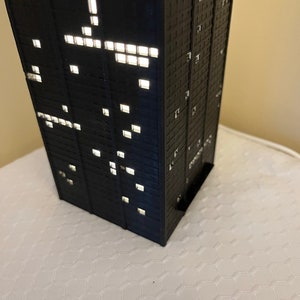 May include: A black model of a skyscraper with windows lit up, creating a pattern of light.