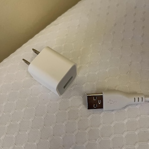 Peut inclure: Un chargeur USB blanc et un c&acirc;ble USB blanc sont pr&eacute;sent&eacute;s sur une surface blanche &agrave; motifs. Le chargeur a deux broches et un port USB. Le c&acirc;ble a un connecteur USB &agrave; une extr&eacute;mit&eacute;.