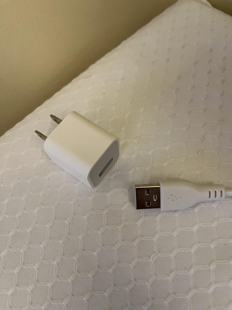 Peut inclure: Un chargeur USB blanc et un c&acirc;ble USB blanc sont pr&eacute;sent&eacute;s sur une surface blanche &agrave; motifs. Le chargeur a deux broches et un port USB. Le c&acirc;ble a un connecteur USB &agrave; une extr&eacute;mit&eacute;.
