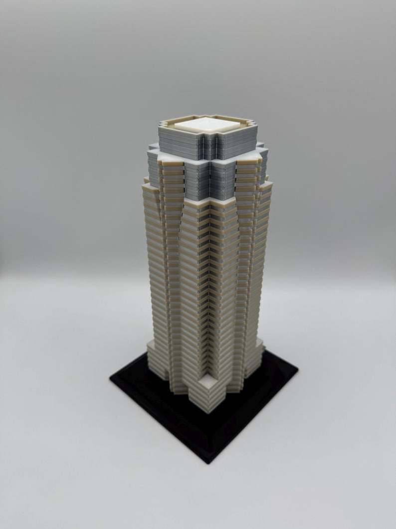May include: A 3D-printed model of a skyscraper. The building is primarily light gray with white and dark gray accents. It has a rectangular base and a detailed facade, showcasing a modern architectural design.