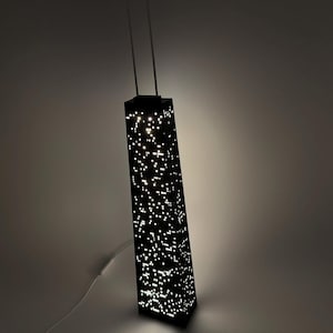May include: A black, rectangular lamp shaped like a skyscraper, with numerous small, illuminated dots creating a city lights effect. The lamp has two thin, vertical supports extending from the top.