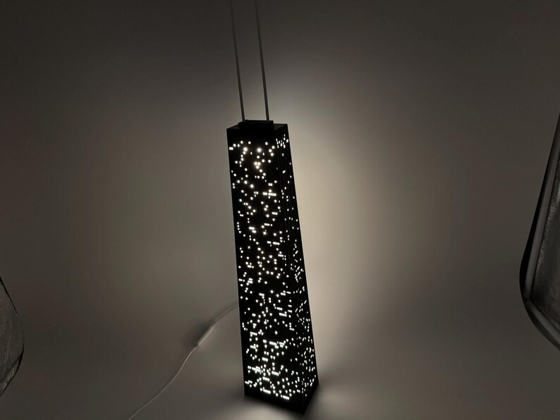 May include: A black, rectangular lamp shaped like a skyscraper, with numerous small, illuminated dots creating a city lights effect. The lamp has two thin, vertical supports extending from the top.