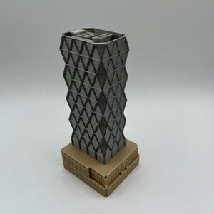 May include: A grey 3D printed model of a skyscraper with a geometric facade. The building has a brown base.
