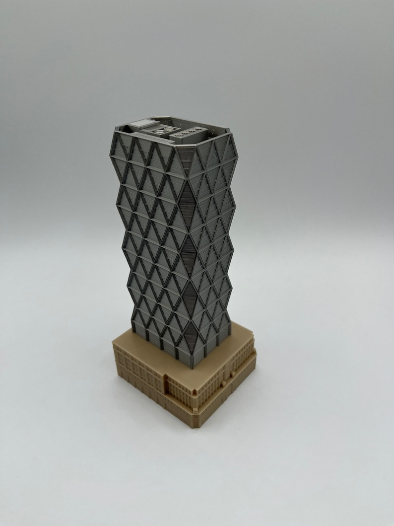 May include: A grey 3D printed model of a skyscraper with a geometric facade. The building has a brown base.