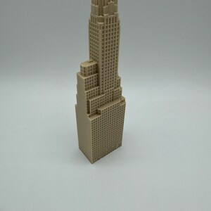 May include: A beige 3D printed model of a tall skyscraper building.