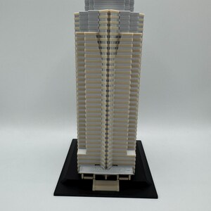 May include: A detailed architectural model of a skyscraper. The building features a beige and gray color scheme with a black base. The model showcases intricate details of the building's facade.