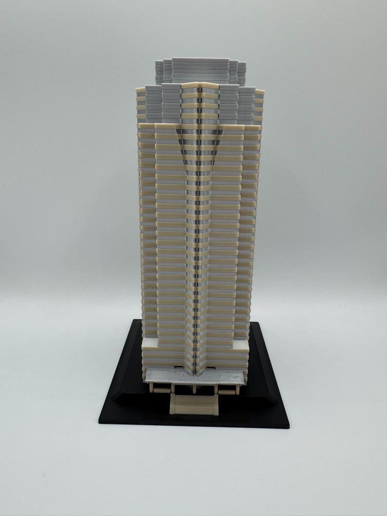 May include: A detailed architectural model of a skyscraper. The building features a beige and gray color scheme with a black base. The model showcases intricate details of the building's facade.